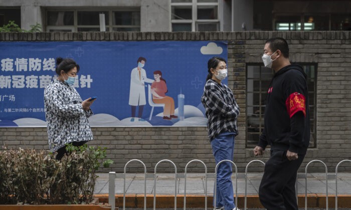 Люди стоят в очереди для сдачи анализа на нуклеиновую кислоту для выявления COVID-19 рядом с плакатом о вакцинации на импровизированном месте тестирования в Центральном деловом районе Чаоян в Пекине, Китай, 27 апреля 2022 года. (Kevin Frayer/Getty Images) | Epoch Times Россия
