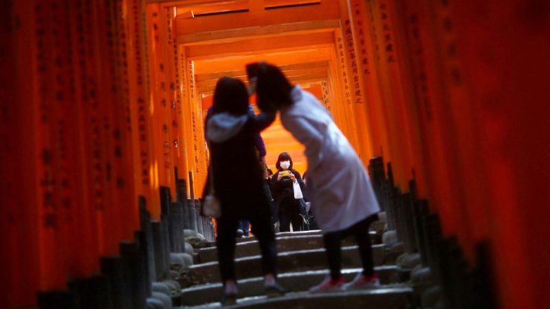 Посетители в масках после вспышки COVID-19 осматривают деревянные ворота тории в синтоистском святилище Фусими Инари Тайша в Киото, Япония, 13 марта 2020 года. (Edgard Garrido/Reuters)  | Epoch Times Россия