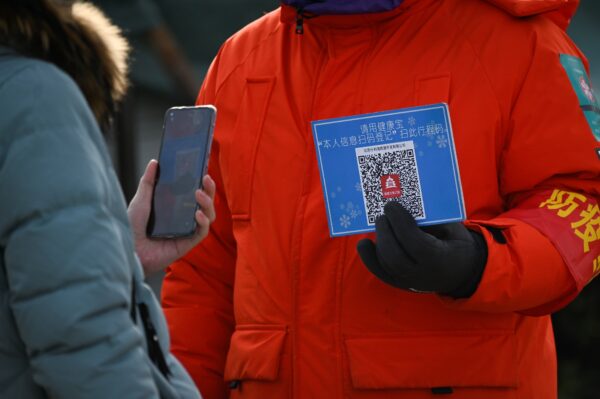 Женщина использует свой мобильный телефон для сканирования кода места проведения мероприятия перед входом на открытый каток в Пекине 12 января 2021 года. (WANG ZHAO/AFP via Getty Images)