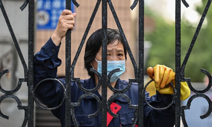 Работница смотрит через забор на территории комплекса во время карантина из-за COVID-19 в районе Цзинань города Шанхая, Китай, 25 мая 2022 года. (Hector Retamal/AFP via Getty Images) | Epoch Times Россия