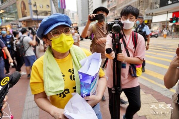 Женщина в жёлтом топе с надписью «Вперёд, Гонконг» раздавала чистые листы формата А4. Полиция пыталась остановить её. (Юй Ган/ The Epoch Times)