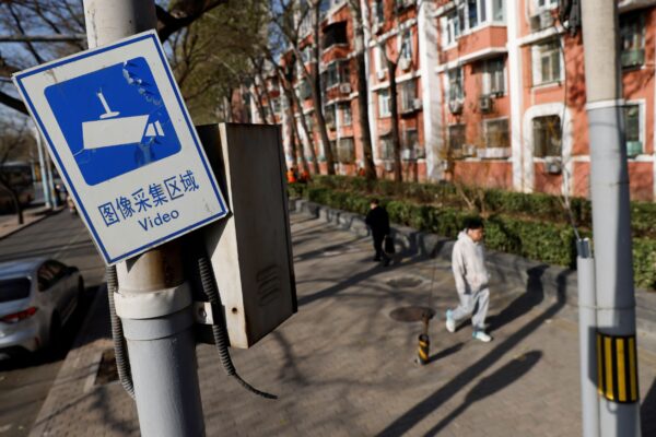 Табличка с надписью о том, что район находится под видеонаблюдением, висит на столбе, пока люди идут по улице в Пекине 25 ноября 2021 года. (Carlos Garcia Rawlins/Reuters)