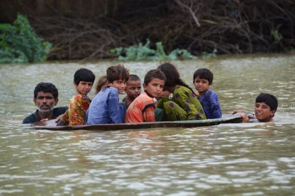 Мужчина (слева) вместе с молодым человеком используют спутниковую антенну, чтобы перевести детей через затопленную территорию после сильных муссонных дождей в районе Джаффарабад, провинция Белуджистан, Пакистан, 26 августа 2022 года. (Fida Hussain/AFP via Getty Images)
