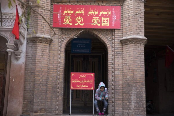 Ребёнок у входа в мечеть, где на красном транспаранте написано «Любите партию, любите страну» в старом районе города Кашгар в регионе Синьцзян на западе Китая, 4 ноября 2017 г. (AP Photo/Ng Han Guan).