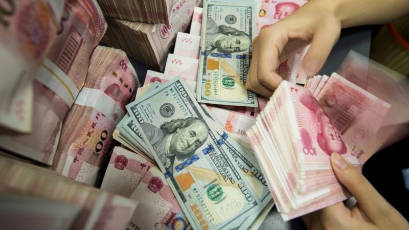 Сотрудник китайского банка пересчитывает банкноты в 100 юаней и доллары США на банковской стойке в Наньтуне в китайской восточной провинции Цзянсу 28 августа 2019 года. (STR/AFP/GettyImages) | Epoch Times Россия
