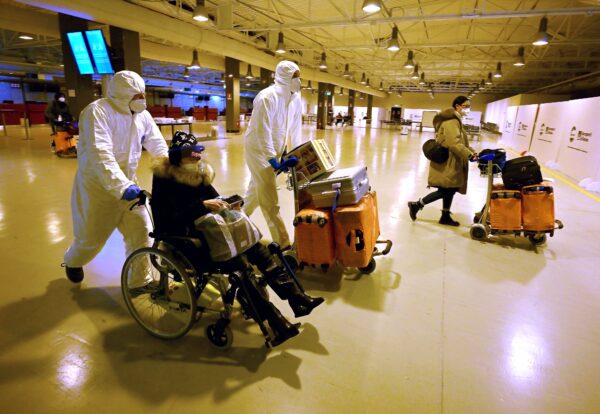 Рабочие в защитных масках и костюмах помогают китайским путешественникам покинуть зал прибытия после тестирования на вирус COVID-19 в международном аэропорту Фьюмичино, недалеко от Рима, 29 декабря 2022 года. (Filippo Monteforte/AFP via Getty Images)