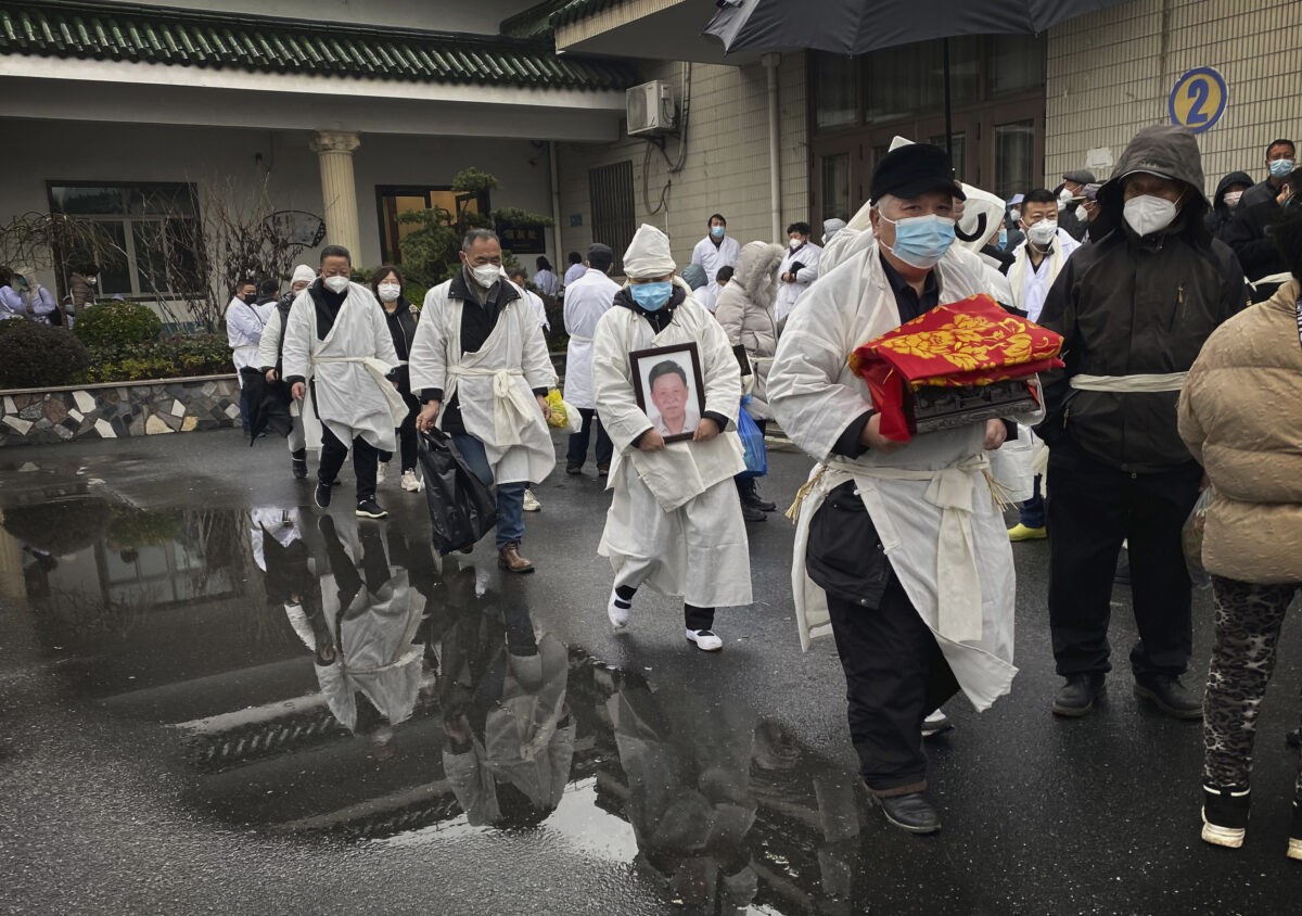 Скорбящий несёт кремированные останки близкого человека в традиционной белой похоронной одежде во время похорон в Шанхае. (Kevin Frayer/Getty Images)