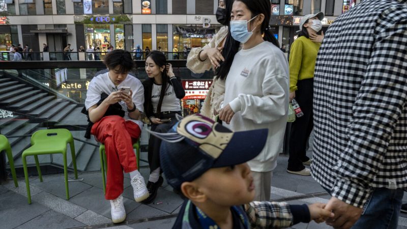 Пара смотрит на мобильный телефон, ожидая столика возле ресторана в оживлённом торговом районе в Пекине 18 апреля 2023 года. (Kevin Frayer/Getty Images)
 | Epoch Times Россия