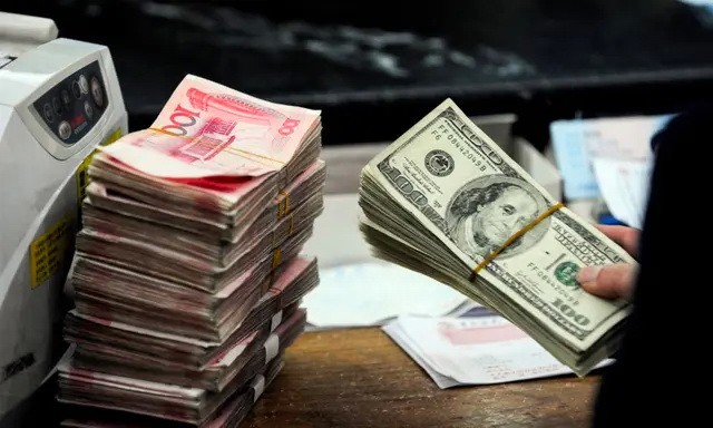 Китайский банковский работник готовится пересчитать пачку долларов США и пачки банкнот в 100 китайских юаней в банке в Хэфэе, провинция Аньхой, Китай, 9 марта 2010 года. (STR/AFP via Getty Images)
 | Epoch Times Россия