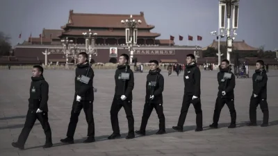 Группа мужчин в чёрных куртках с камерами и планшетами идёт по площади Тяньаньмэнь в Пекине.