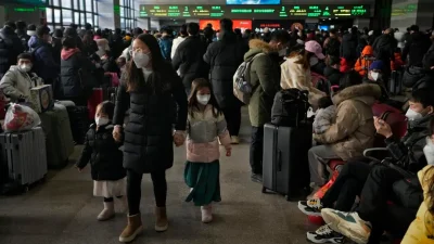 Толпа людей в масках на Западном железнодорожном вокзале Пекина, мать ведёт детей за руки среди путешественников.