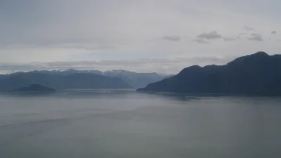 Панорамный вид на суровый пейзаж острова Врангеля: спокойная гладь воды и темные очертания гор под облачным небом.