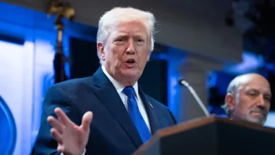 Дональд Трамп выступает за трибуной в Белом доме на фоне синего освещения, жестикулируя рукой во время речи о введении новых импортных тарифов в феврале 2026 года.