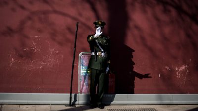 Военизированный охранник в форме у красной стены Запретного города в Пекине жестом запрещает съёмку.