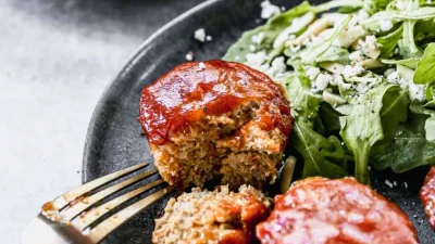 Подача мясных мини-рулетов (маффинов) на темной тарелке с салатом из рукколы и сыром фета.