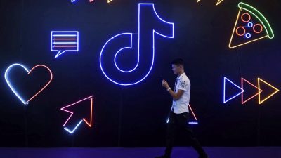 Человек проходит мимо неонового логотипа Douyin в Китае