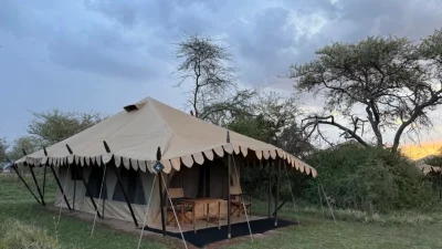 Роскошная сафари-палатка (нюмба) с террасой в национальном парке Серенгети на закате.