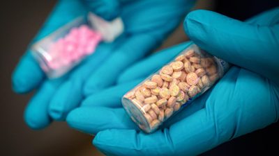 Руки в синих перчатках держат флаконы с разноцветными таблетками фентанила