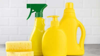 Желтые бутылки с чистящими средствами и губки для уборки дома