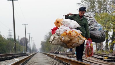 Китайский рабочий-мигрант с устройством для сбора мусора идёт по железной дороге в Ухане, провинция Хубэй, Китай, 6 декабря 2004 года.