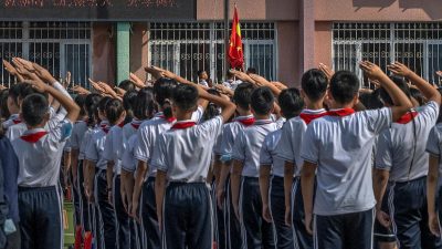 Ученики отдают честь, когда во время церемонии в первый день нового учебного года в начальной школе в Пекине поднимают государственный флаг.