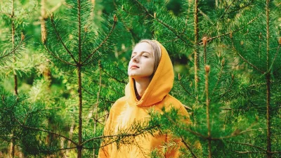 Девушка с закрытыми глазами наслаждается звуками природы в хвойном лесу