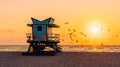 Разноцветная спасательная вышка на песчаном пляже Майами-Бич на фоне рассвета над океаном.