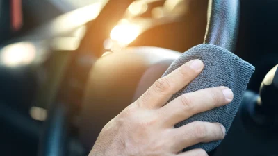 Водитель протирает тряпкой руль автомобиля.