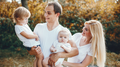 Счастливая семья с двумя маленькими детьми на прогулке в парке