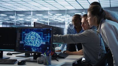 Команда IT-специалистов обсуждает код и визуальную схему ИИ на мониторах