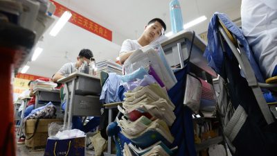 Китайский студент за партой с огромными стопками книг и тетрадей