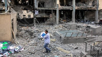 Мужчина идет среди руин разрушенного здания в Иране с документами в руках