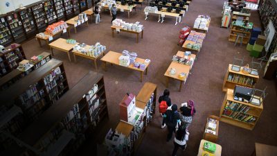 Школьники выбирают книги в библиотеке среди стеллажей и столов