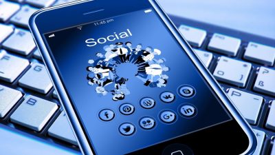 Смартфон с открытыми иконками социальных сетей на клавиатуре компьютера, иллюстрирующий проблему цифровой аддикции у подростков.