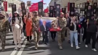 Группа людей в камуфляже несет флаг с портретом Евгения Пригожина на шествии «Бессмертный полк» в Санкт-Петербурге