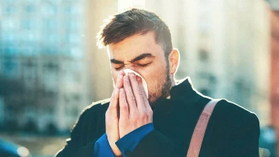 Мужчина с симптомами сезонной аллергии чихает в платок на улице