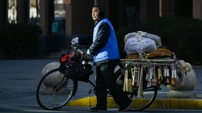 Продавец, толкающий велосипед, готовится перейти дорогу в Пекине, 3 января 2024 года.
