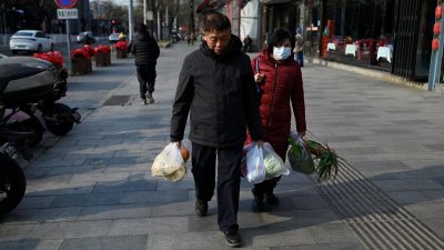 Пожилые мужчина и женщина с продуктами в руках проходят мимо ресторана в Пекине, 22 декабря 2025 года.