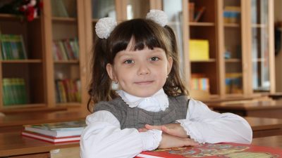 Ученица начальных классов сидит за партой с учебником в школьном кабинете.